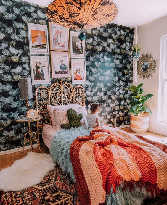 a maximalist sleeping space with a dark accent wall, a rattan bed, a catchy pendant lamp and bright textiles for creating a mood