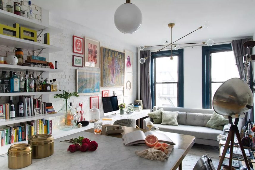 a maximalist space with a brick wall, open shelves, neutral furniture, metallic accents and a colorful gallery wall is cool