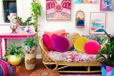 a maximalist space with a hot pink table, a rattan sofa, colorful textiles and pillows, ottomans and a gallery wall is wow