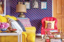 a maximalist space with bold printed walls, a gallery wall, a yellow sofa, a red chair, a blue ottoman and printed pillows for more fun