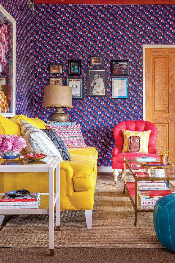 a maximalist space with bold printed walls, a gallery wall, a yellow sofa, a red chair, a blue ottoman and printed pillows for more fun