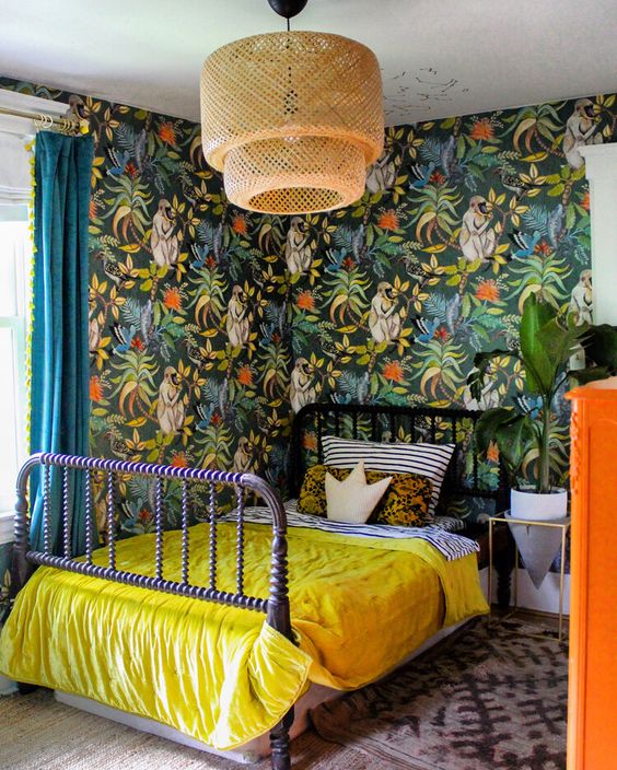 a maximalist space with bold wallpaper walls, a purple bed, a rattan lamp, an orange dresser and bright bedding is chic