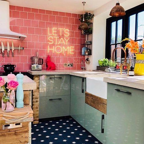 a modern maximalist kitchen with aqua cabinets, a pink tile backsplash, a neon light, a black window frame and colorful vases