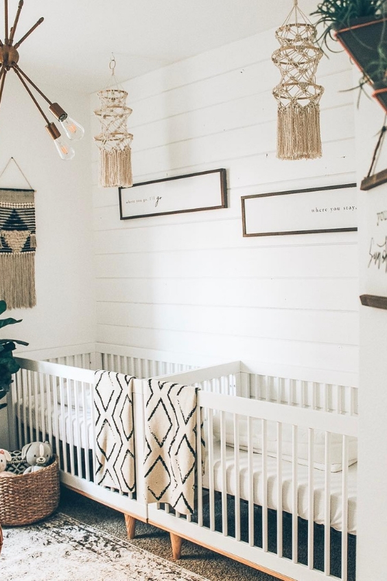 a neutral boho twin nursery with white walls, white cribs, macrame hangings, printed textiles and some greenery