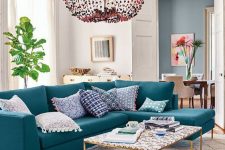 a pretty living room with a turquoise sectional, a cool coffee table, a beaded chandelier and a potted plant plus artworks
