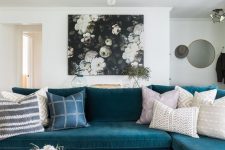 a pretty living room with a turquoise sectional, a dark floral artwork, a marble coffee table and a gold chandelier