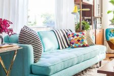 a pretty living room with a turquoise sofa, a modern storage unit, a coffee table and touches of gold here and there