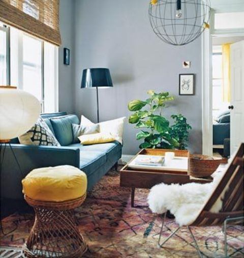 a pretty living room with grey walls, a turquoise sofa, some rattan and wooden furniture, a printed rug and a potted plant