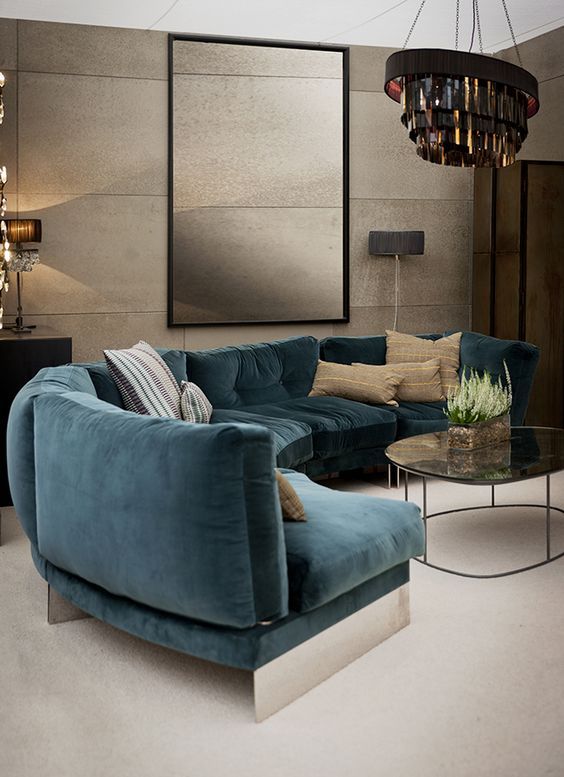 a refined living room with a curved turquoise sofa, a bold chandelier, tan walls with a texture and chic lamps