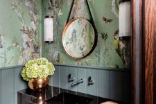 a refined maximalist bathroom with green flora and fauna wallpaper, a black stone vanity, a mosaic tile floor and a round mirror