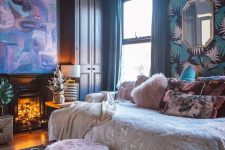 a refined maximalist bedroom with dark walls, a printed ceiling, a fireplace with lights, a statement artwork and a daybed with pillows