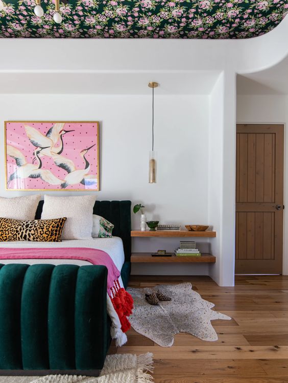 a stylish maximalist bedroom with a floral ceiling, a dark green velvet bed, a bold artwork and pretty rugs plus pendant lamps