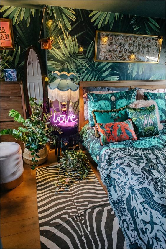 a tropical maximalist bedroom with an accent wall, a gilded bed, a mirror and a neon light plus string lights and bold printed textiles here and there