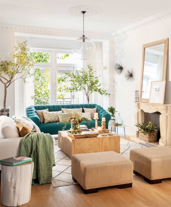 a welcoming living room with a fireplace, neutral furniture, potted trees and a turquoise sofa for a bold color statement