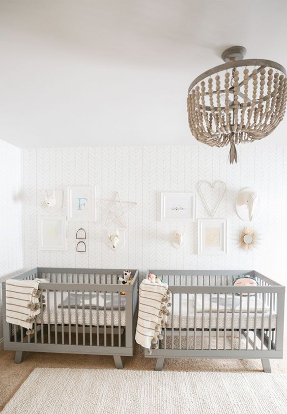 an airy twin nursery with an accent wall, grey crib, a wooden bead chandelier, neutral and printed bedding and a gallery wall