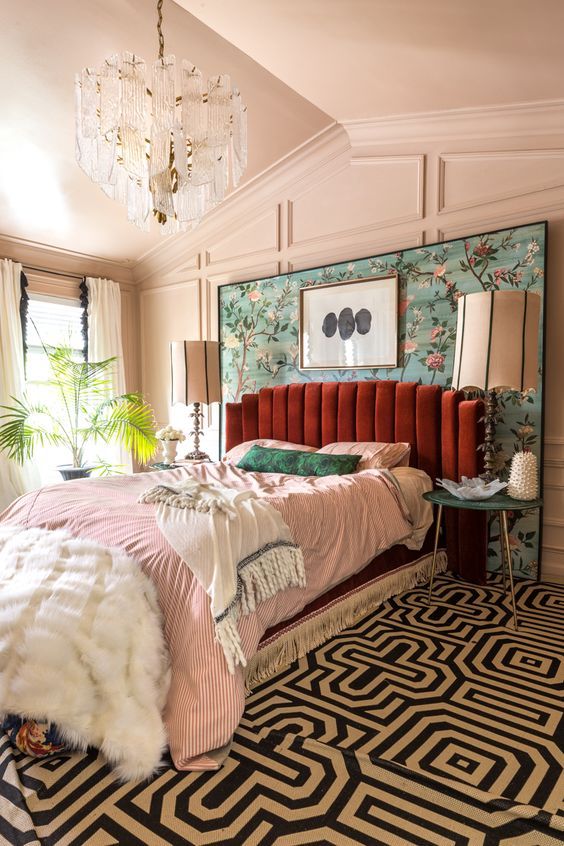 an elegant maximalist bedroom with paneled walls, a burgundy velvet bed, a printed carpet, pastel bedding and a lovely crystal chandelier