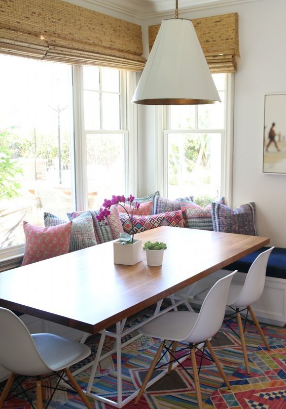 a bright boho dining space with a corner window, shades, a corner banquette seating, a dining table and white chairs