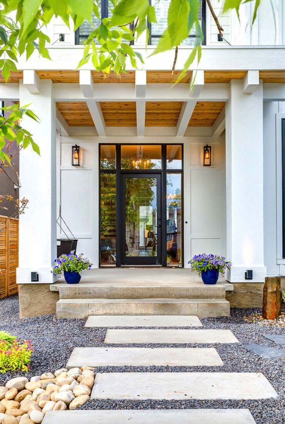 a modern and fresh porch with a glass door, bold blue planters with lilac blooms and a hanging chair plus lanterns on the walls