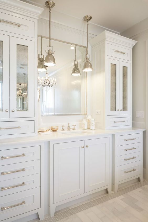 an elegant and stylish creamy bathroom made with vintage kitchen cabinets, a mirror in a metallic frame and vintage pendant lamps