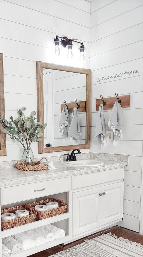 a stylish white bathroom with planked walls, a large white vanity made of kitchen cabinets, a grey stone counterop and mirrors in wooden frames