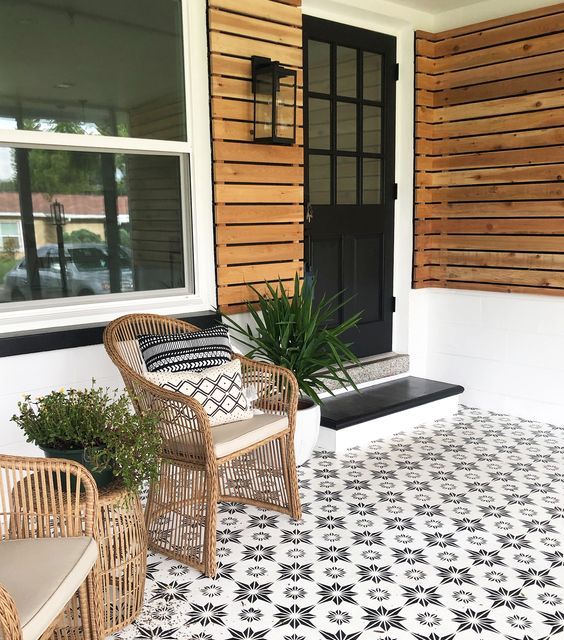 a modern porch clad with pretty star-patterned tiles, with rattan chairs, potted greenery and a black door and steps is a chic idea