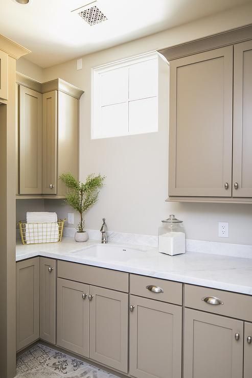 a lovely tan laundry with shaker kitchen cabinets, a white countertop, a small window and a printed rug is cool and fresh