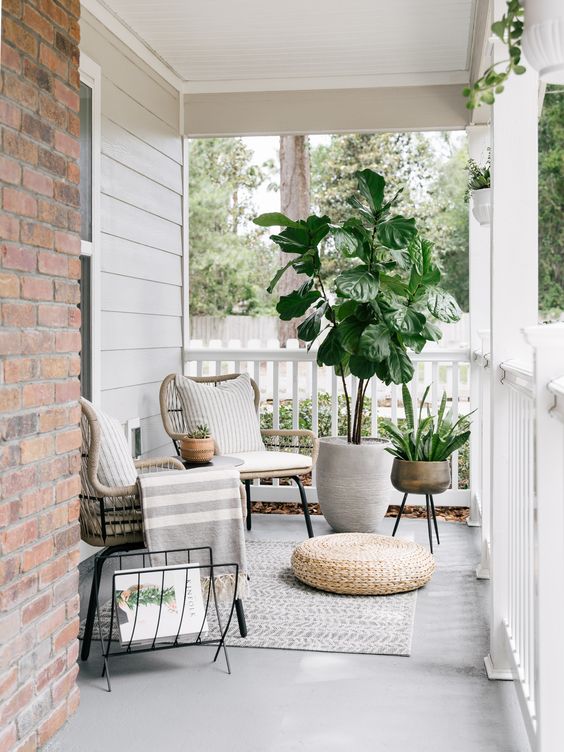a modern porch with rattan chairs, a jute pouf, potted plants, a magazine stand and some neutral textiles is very chic
