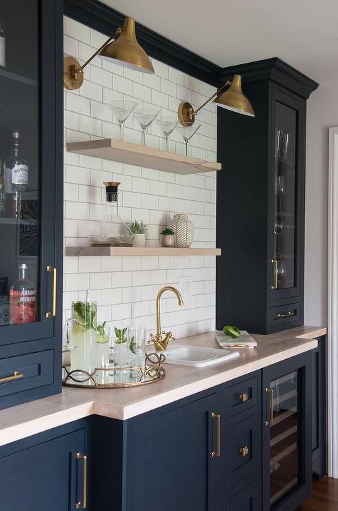 a large navy home bar done with shaker style kitchen cabinets, a blush countertop, open shelves and brass touches for more elegance