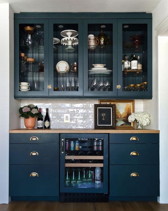 an elegant home bar done with navy kitchen cabinets, glass and usual ones, with a wine cooler and a subway tile backsplash plus a butcherblock countertop
