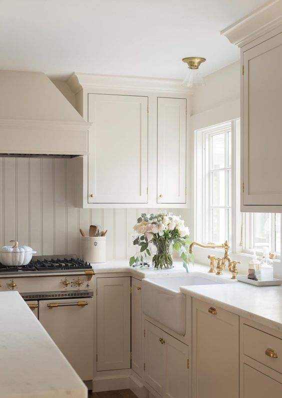 a beautiful creamy modern country kitchen with vintage-inspired cabinetry, a planked backsplash, gold touches and neutral countertops