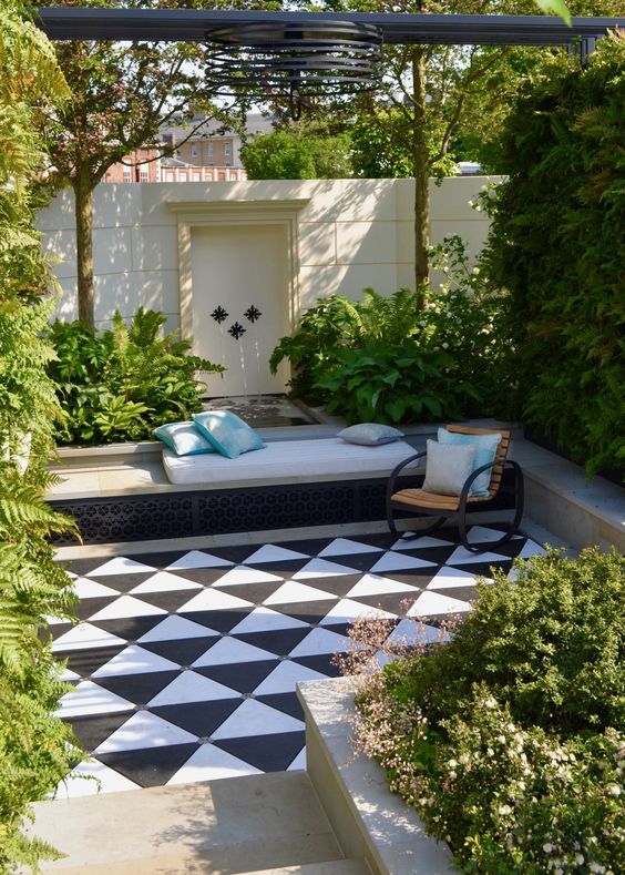 a beautiful sunken terrace with black and white tiles on the floor, built-in benches of concrete, a fountain and lots of greenery