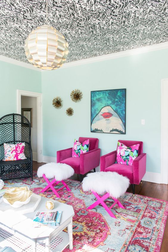 a bold and whimsical living room with a patterned ceiling, hot pink chairs and stools, a bold printed artwork and a bold printed rug