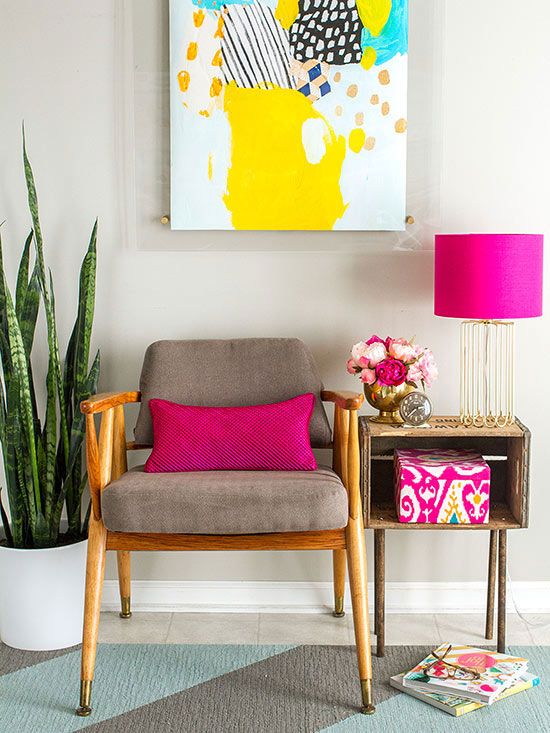 a bold interior with a grey chair, a crate side table, a potted plant, a bright artwork and touches of hot pink in accessories