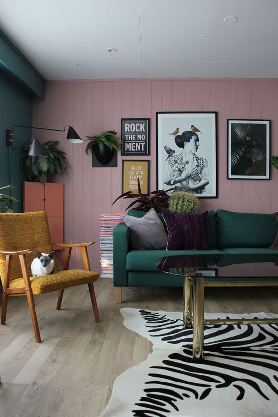 a bold living room with a pink planked accent wall, a dark green sofa and a wall, a mustard chair, some greenery and touches of black for drama