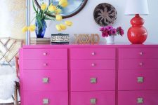 a bold space with a hot pink knob dresser, a zebra rug, a chic chandelier, a round mirror and a table lamp with a red base