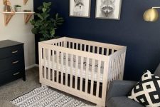 a catchy modern nnursery with a navy accent wall, a grey rocker chair, a white crib, a black dresser, a mini gallery wall and shelves