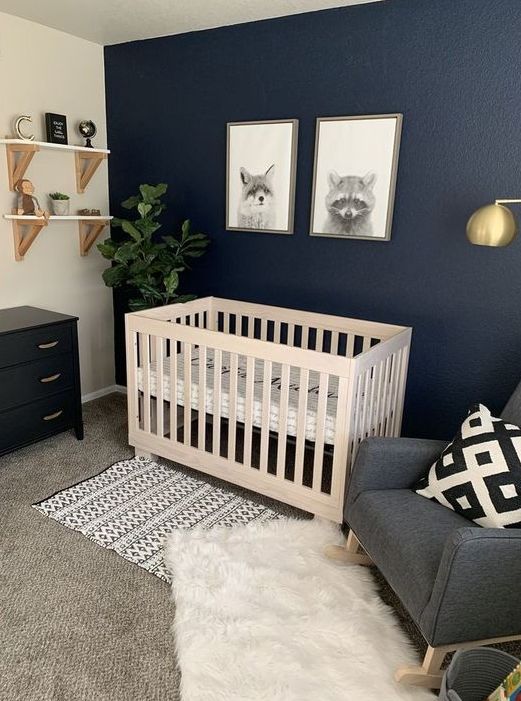 a catchy modern nnursery with a navy accent wall, a grey rocker chair, a white crib, a black dresser, a mini gallery wall and shelves