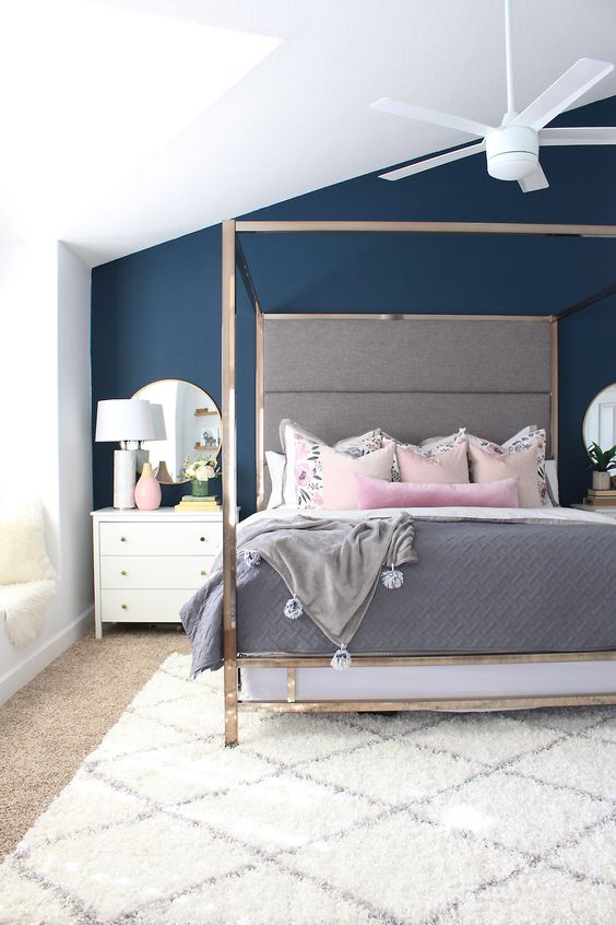 a chic attic bedroom with a navy accent wall, a canopy bed, pretty bedding, layered rugs and chic nightstands is wow
