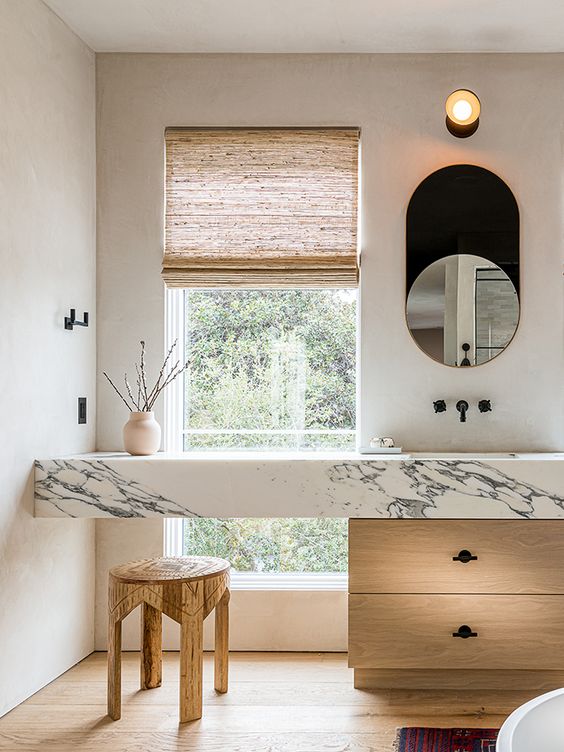 a chic contemporary bathroom with a light-stained and marble vanity, a wooden stool and some decor looks refined and beautiful