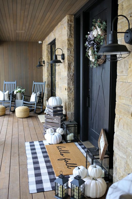 a chic farmhouse porch with navy rockers and white pillows, a plaid rug, crates and lots of pumpkins, a wreath and blooms for the fall