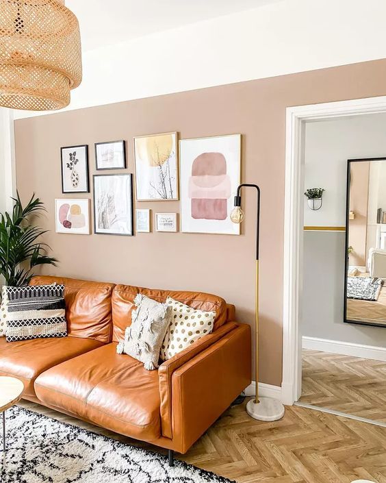 a chic living room with a blush accent wall, an amber leather sofa, a gallery wall, printed pillows and a rug plus a woven pendant lamp