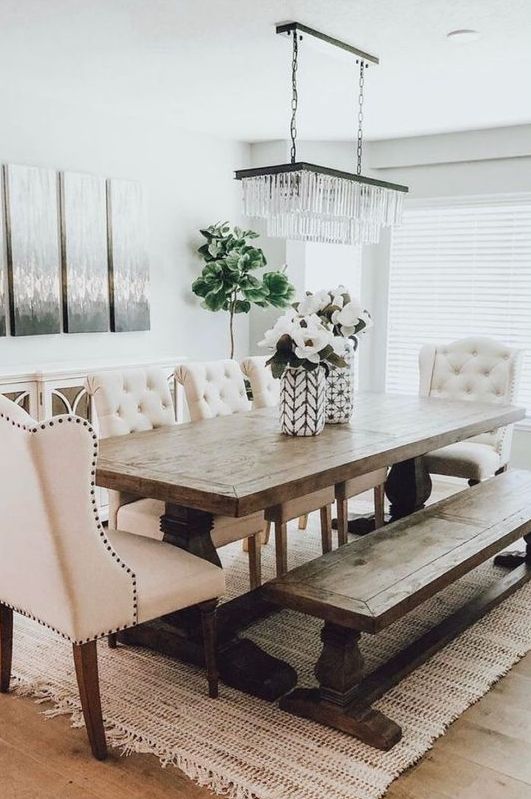 un comedor de campo moderno y elegante con paredes blancas, una mesa de madera vintage y un banco, sillas con mechones y una hermosa lámpara de araña de cristal