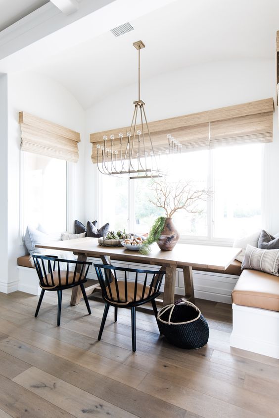 un espacio de comedor de campo moderno y elegante con un asiento de banqueta incorporado, una mesa manchada, sillas negras y cortinas tejidas