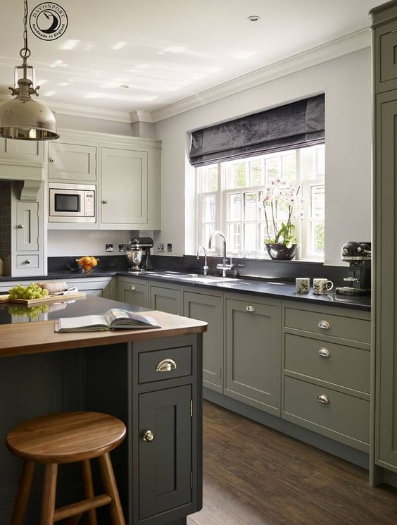 a chic modern country kitchen in olive green, with black and butcherblock countertops, a vintage pendant lamp and shiny knobs