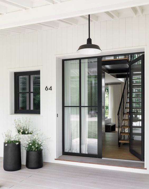a chic modern entrnace with glass doors, a black pendant lamp, black and white planters with blooms and numbers