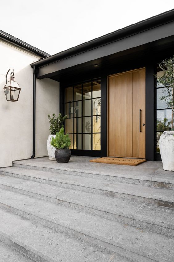 a chic modern front porch with potted greenery in black and white planters, a glazed wall and a heavy wood clad door