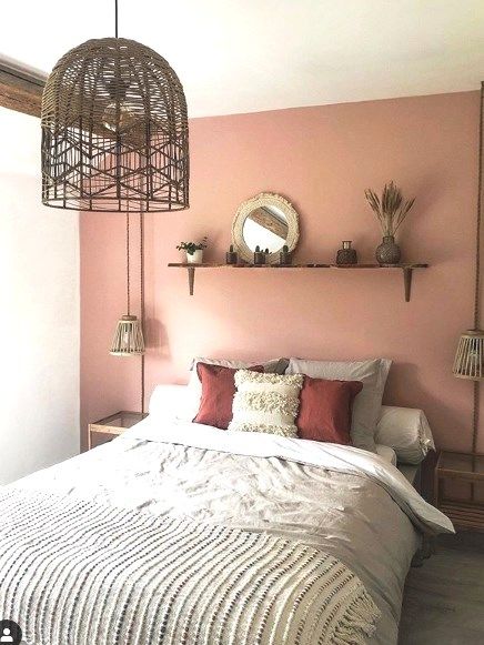 a cool boho bedroom with a pink accent wall, a comfy bed with pretty bedding, a little shelf with some decor and woven pendant lamps