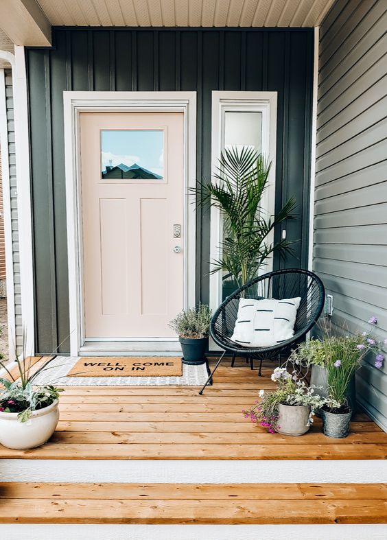 a cool modern porch with a blush door, a black chair, potted plants and blooms and layered rugs is a cool and chic space