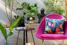 a cool outdoor nook with a woven hot pink chair, a side table, a cushion, potted plants and beautiful Asian-inspired decor
