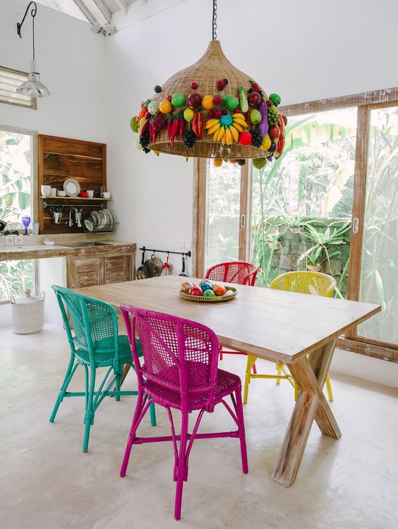 a crazy boho eat-in kitchen with whitewashed furniture, a shabby trestle table, a hot pink, turquoise, yellow and red chair and a jaw-dropping pendant lamp